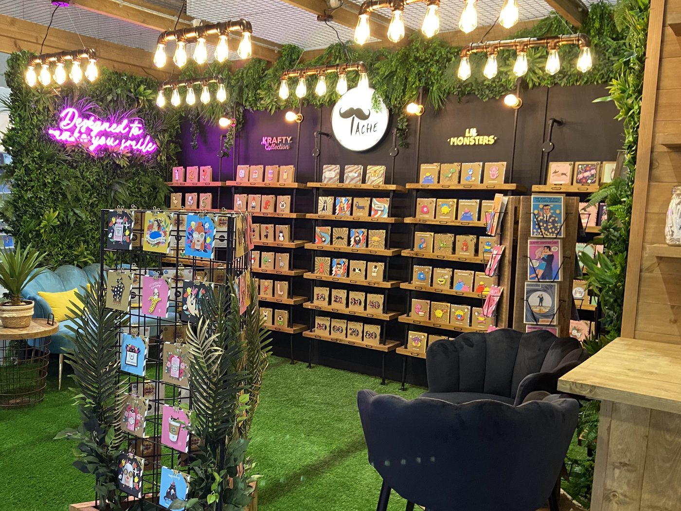 Tache’s trade-show stand, with the round Tache logo and the Krafty Collection and Lil Monsters range signs above shelves of cards
