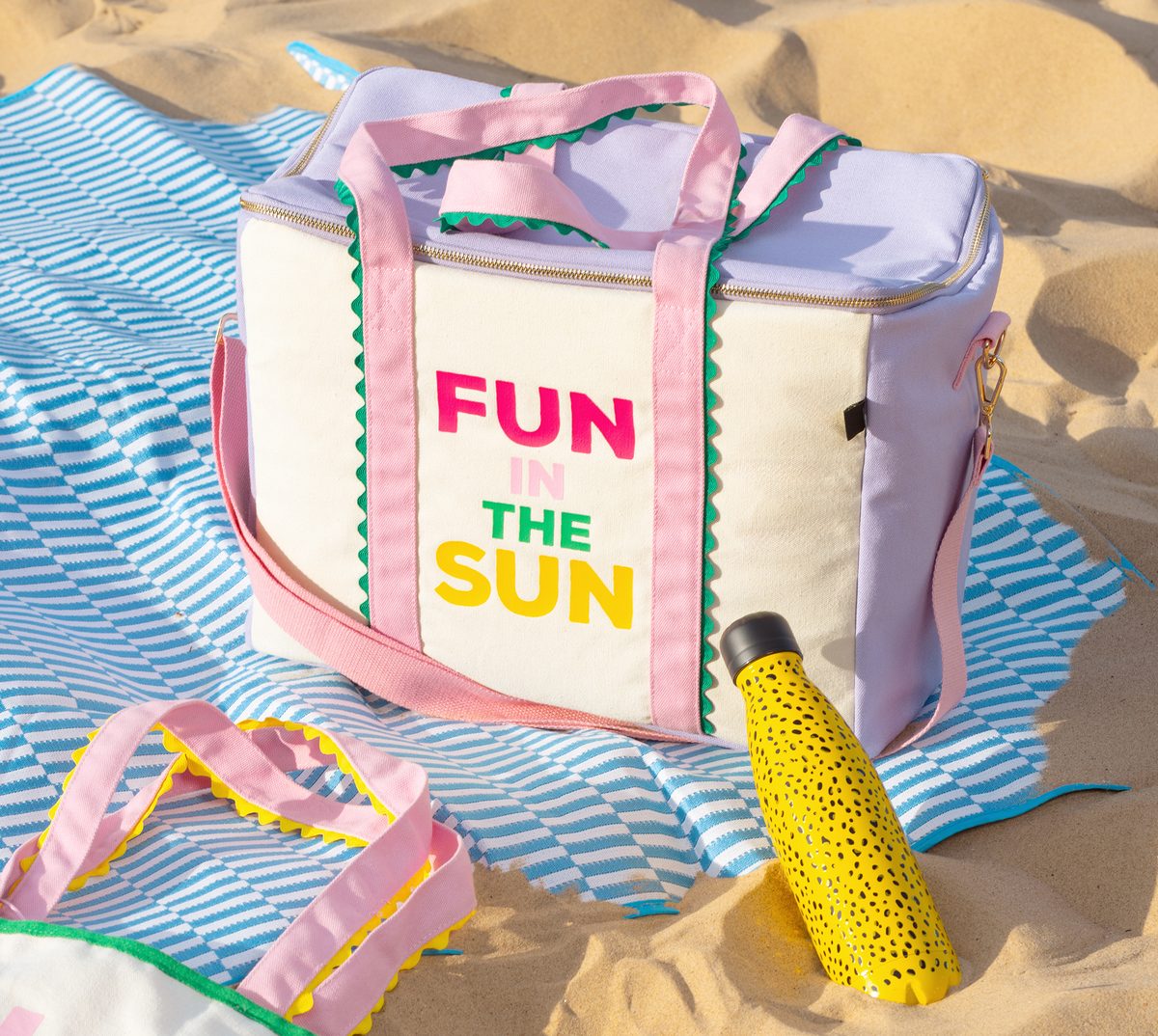 A “Fun in the sun” cooler bag, a tote and a spotted water bottle on a striped beach blanket