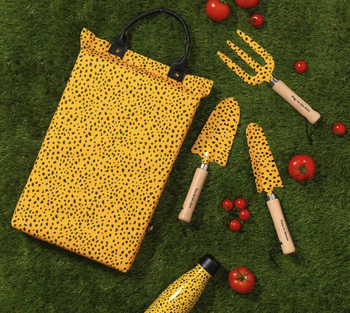 A spotted yellow garden kneeler, hand tools and water bottle laid out on grass with tomatoes